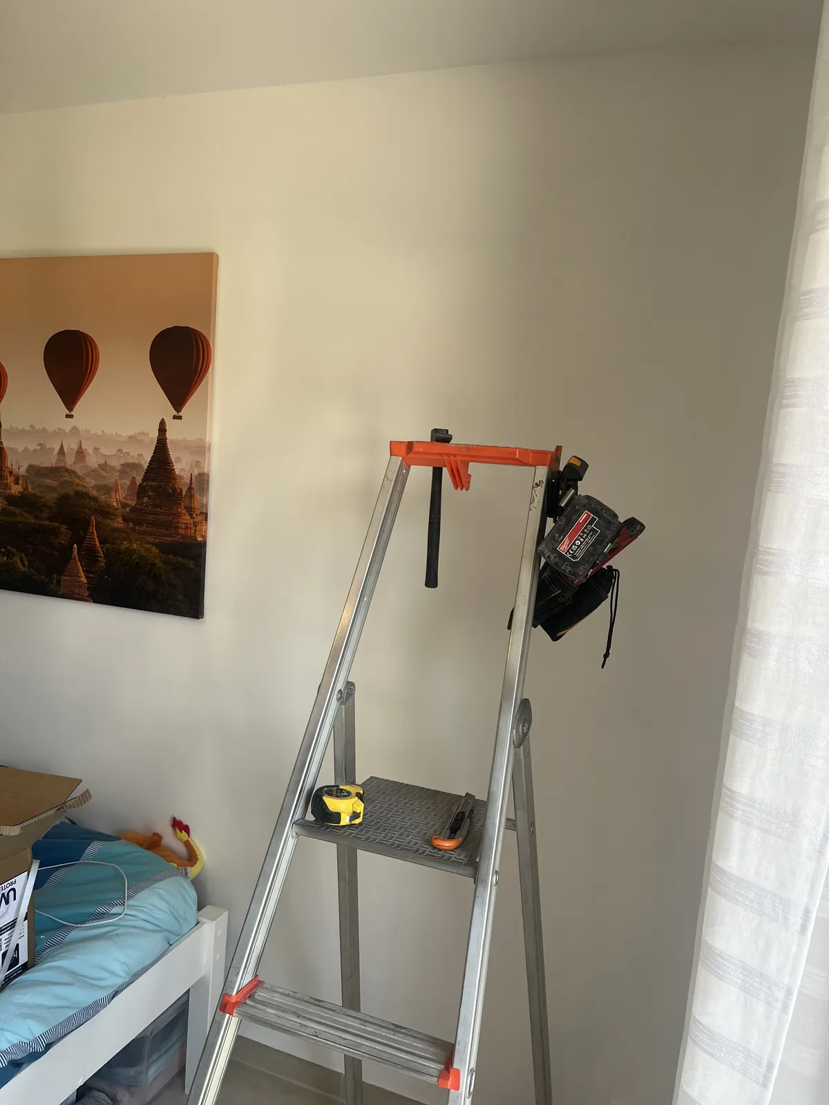 Mur avant installation du climatiseur, avec un escabeau entre un tableau et une fenêtre