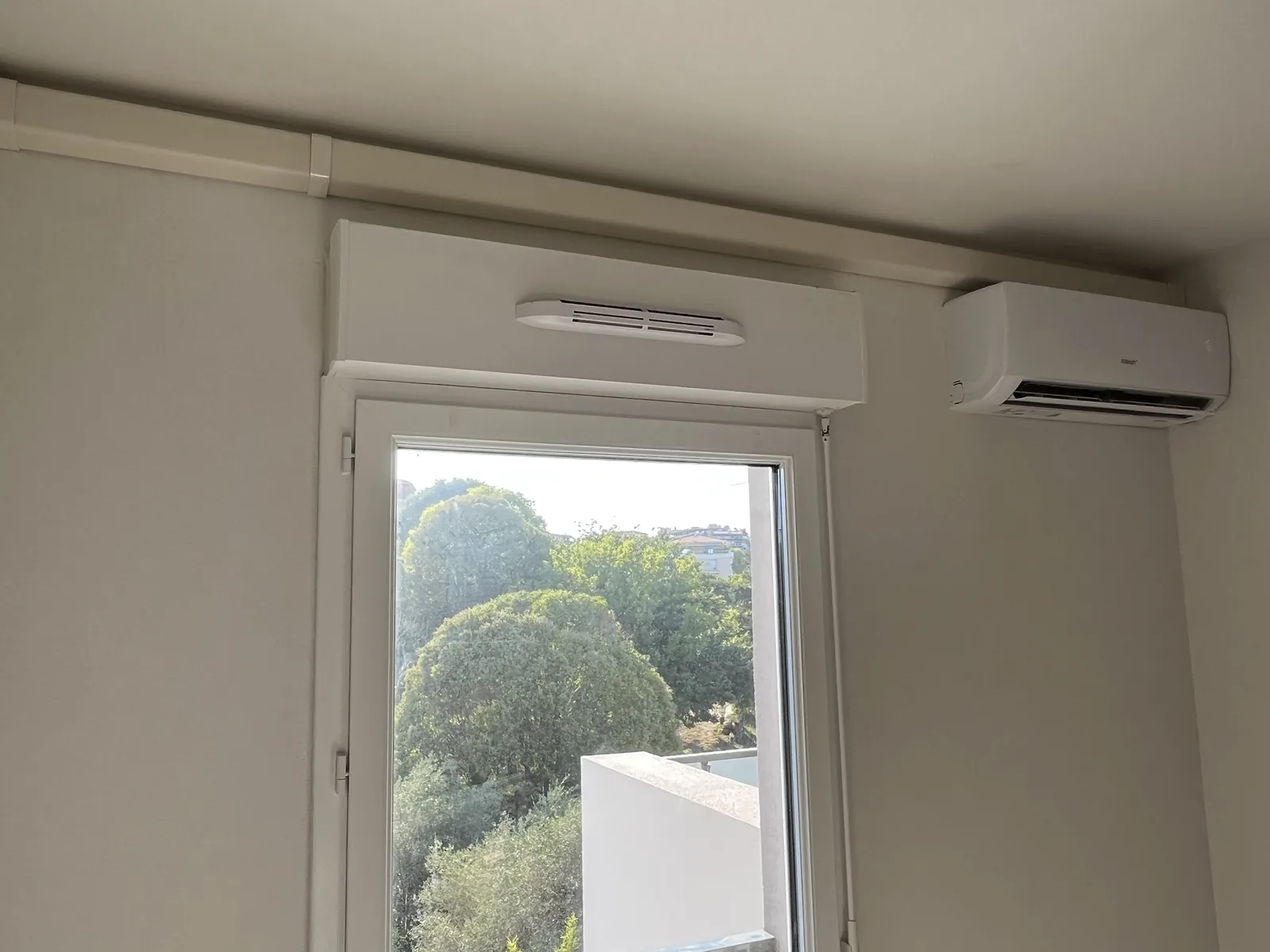 Climatiseur mural à droite d’une fenêtre avec les liaisons dissimulées dans une goulotte blanche en partie haute