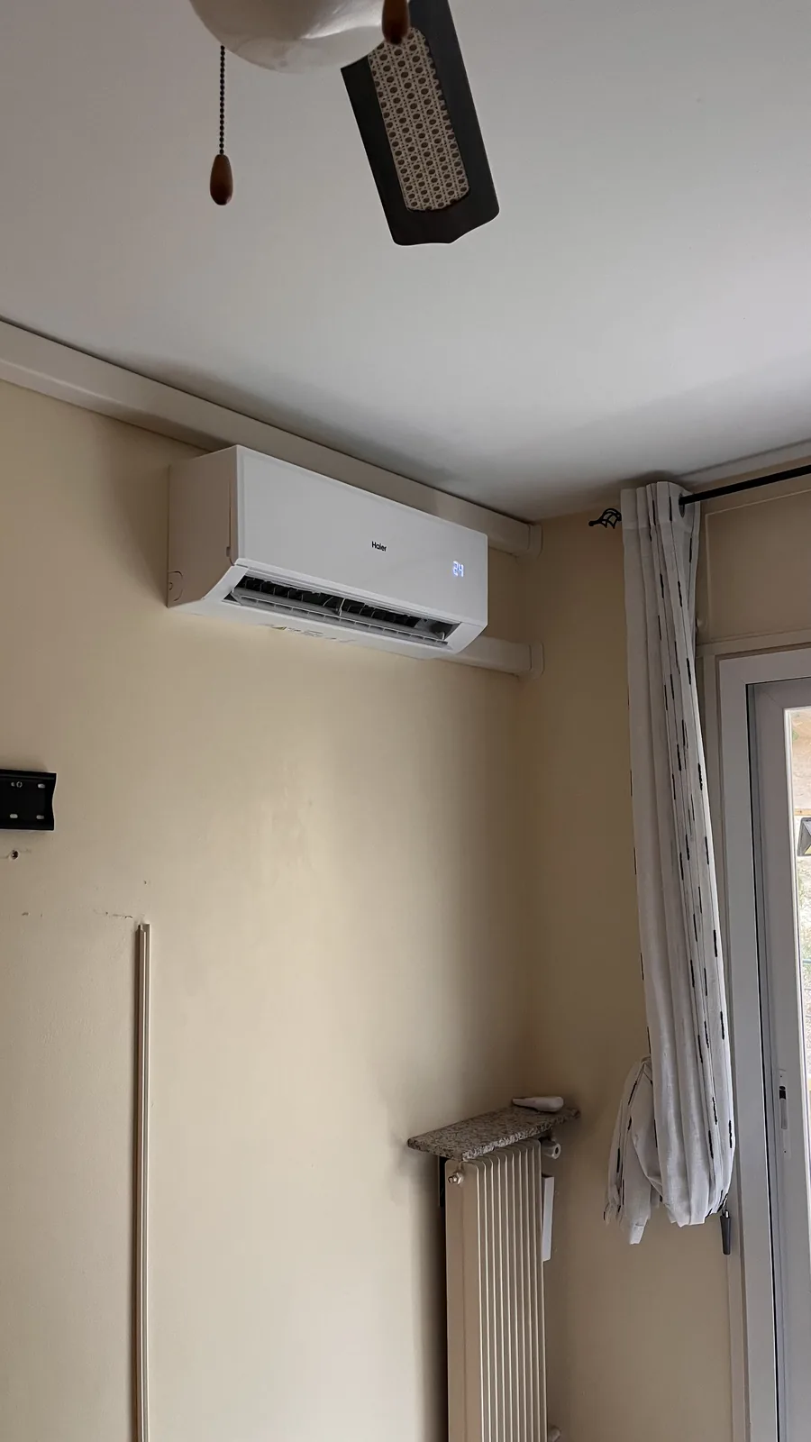 Climatiseur mural Haier dans une pièce aux murs clairs, avec goulottes jusqu’à l’angle près de la fenêtre