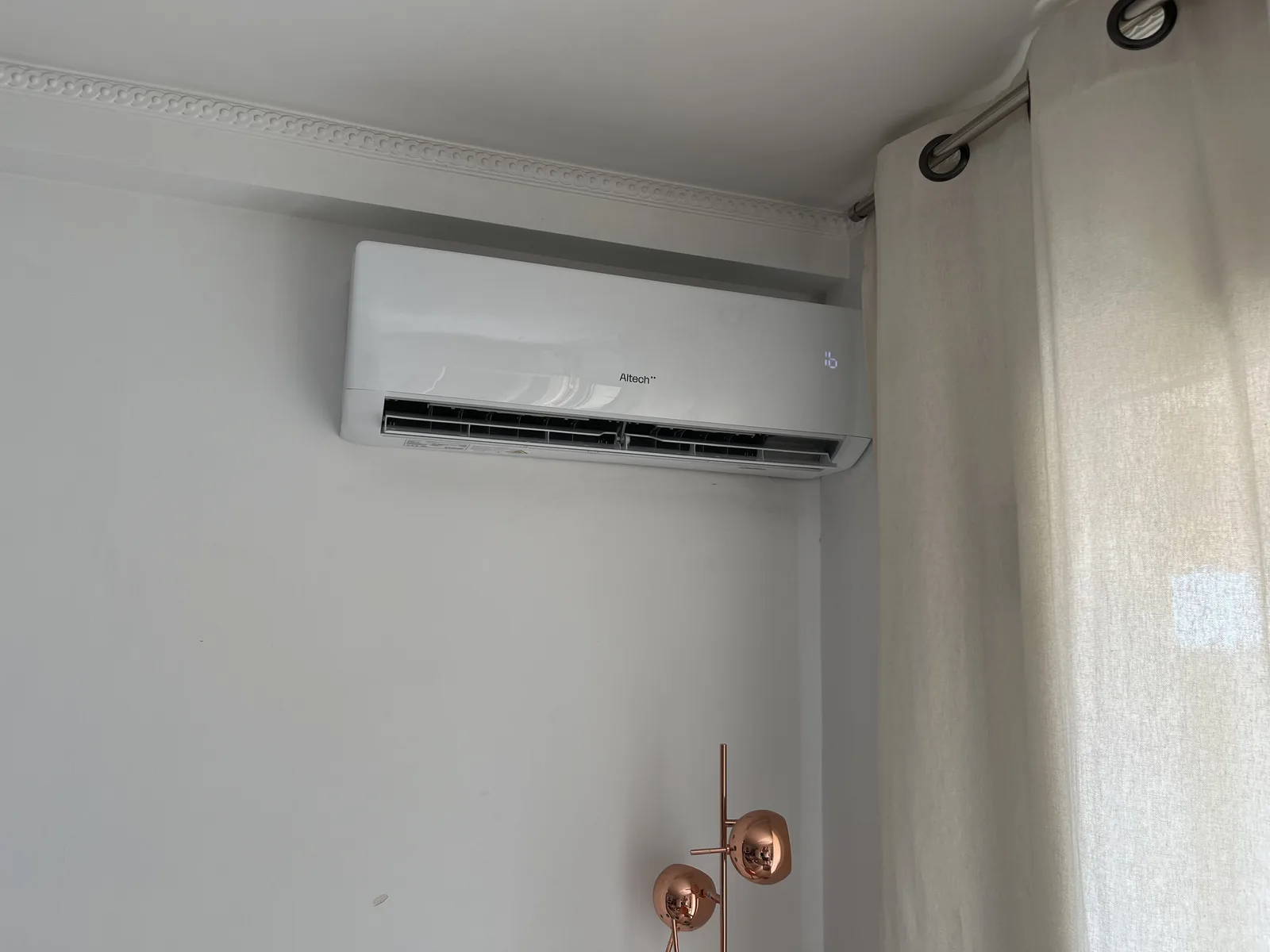 Climatiseur mural Altech installé près d’un rideau, sous les moulures du plafond