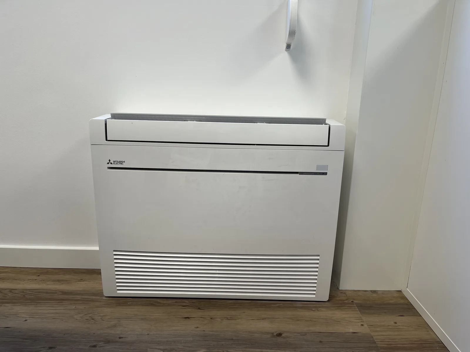 Console de climatisation Mitsubishi Electric posée en partie basse d’un mur sur un sol imitation bois