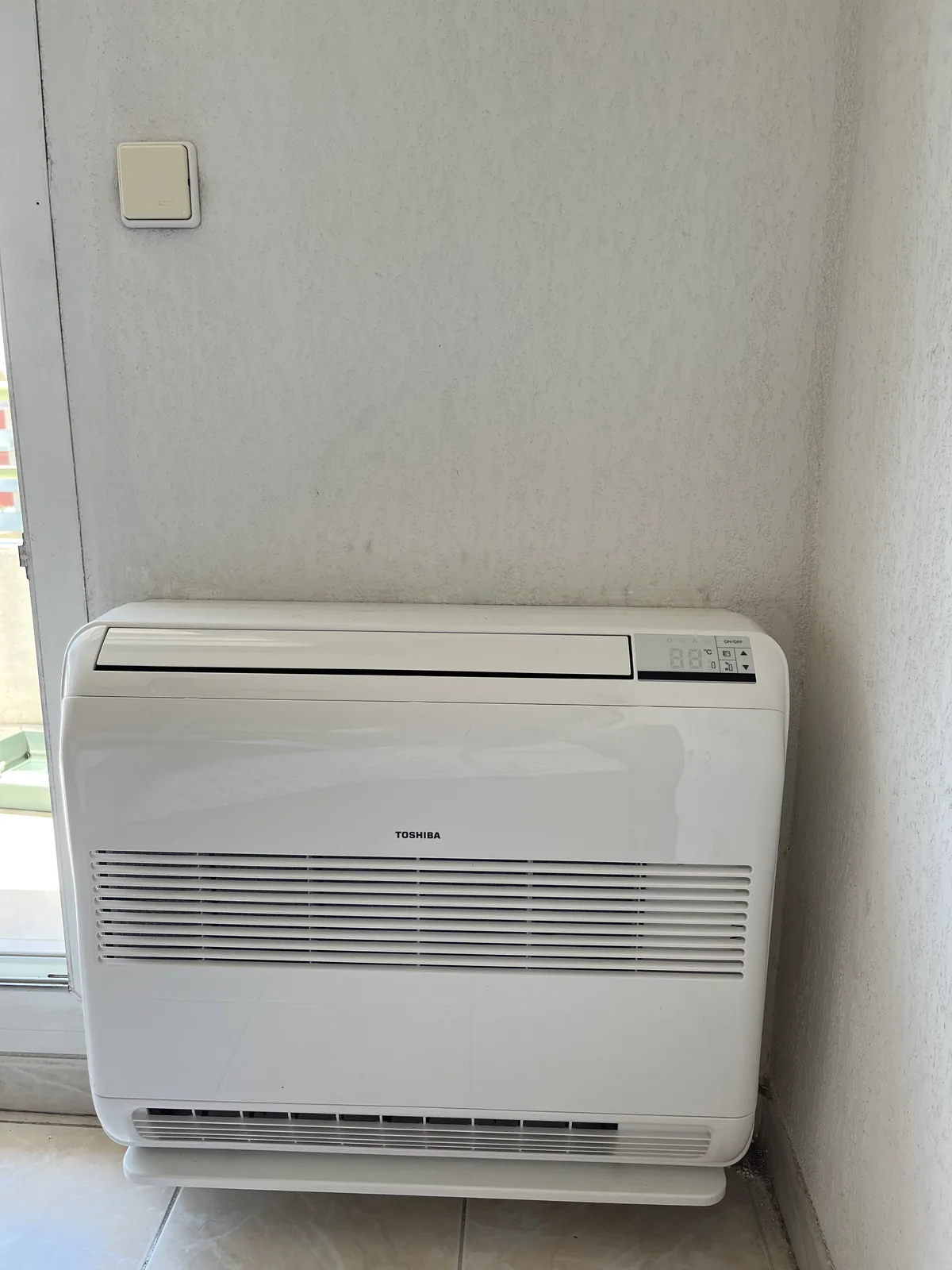 Console de climatisation Toshiba installée au sol dans un angle à côté d’une baie vitrée