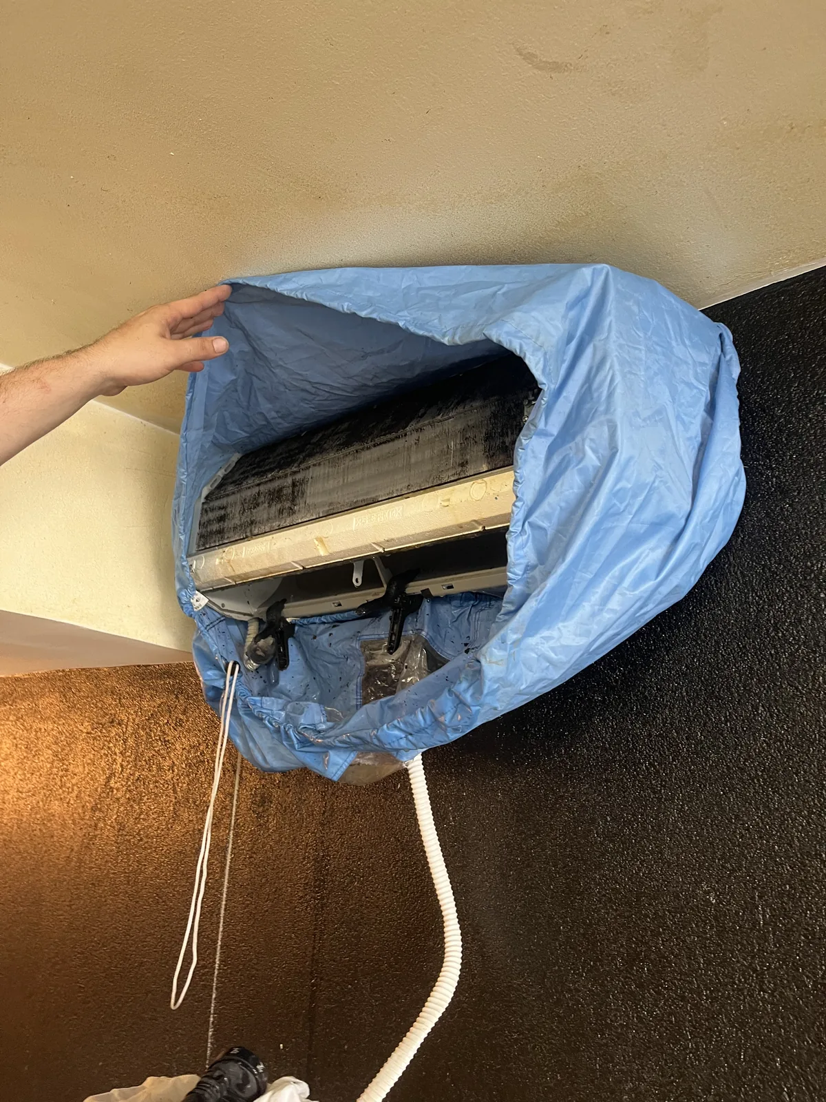 Unité intérieure de climatisation ouverte, entourée d’une housse de protection bleue avec tuyau d’évacuation