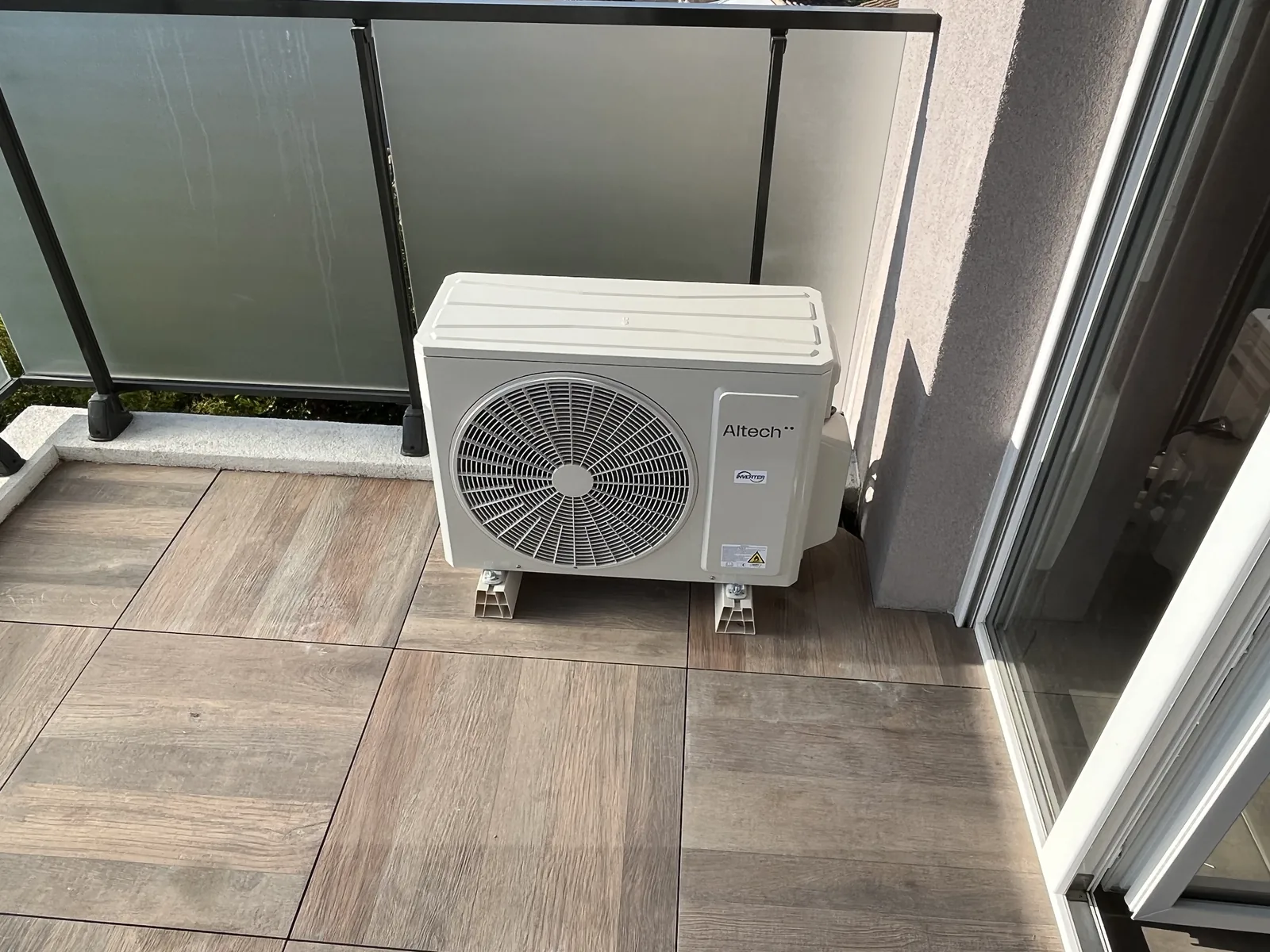 Groupe extérieur Altech sur deux supports, sur un balcon carrelé avec garde-corps vitré