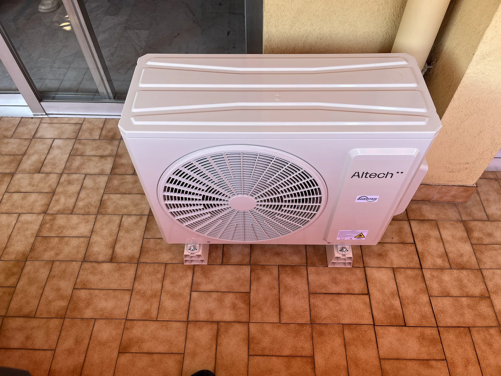 Groupe extérieur Altech posé sur deux supports blancs sur une terrasse carrelée
